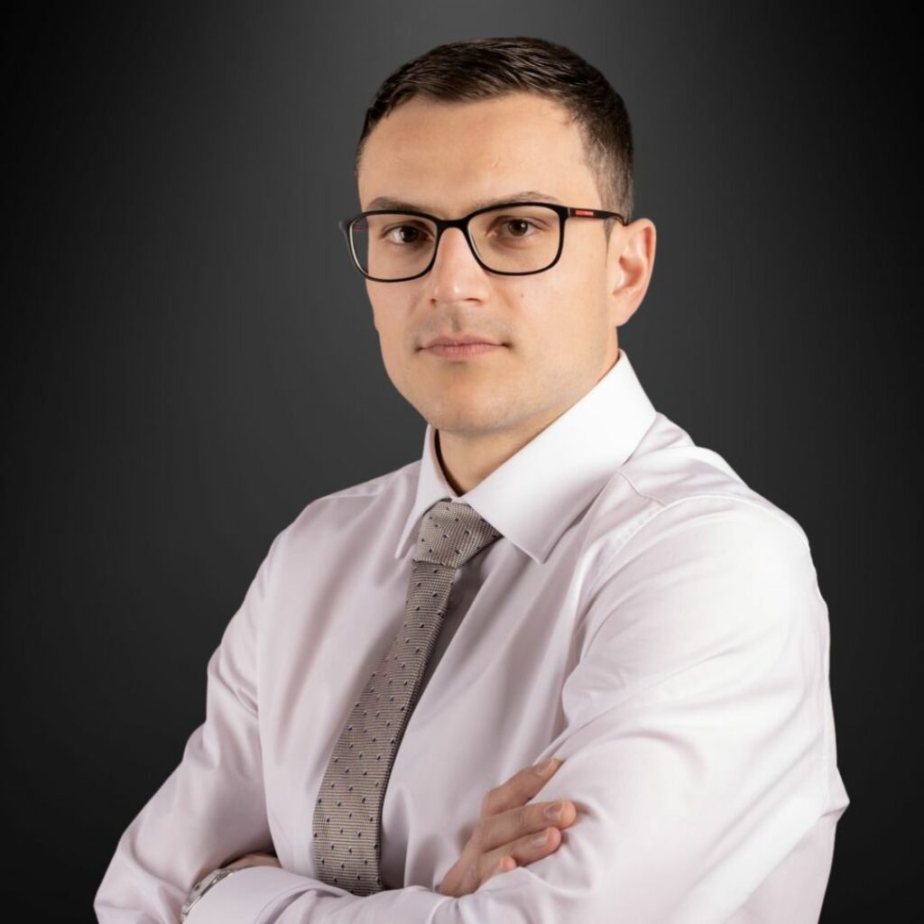 Porträt eines professionellen Rechtsanwalts in Tirol mit weißer Hemdbluse und grauer Krawatte vor einem dunklen Hintergrund, der Kompetenz und Seriosität ausstrahlt.